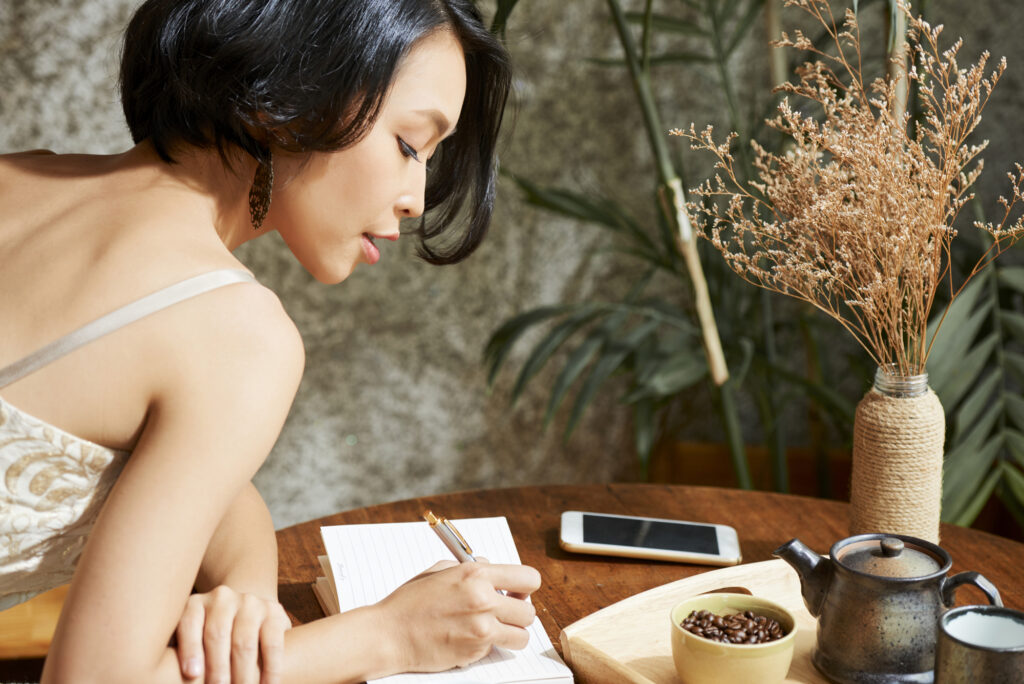 Woman writing in her journal to help with eliminating negative thoughts
