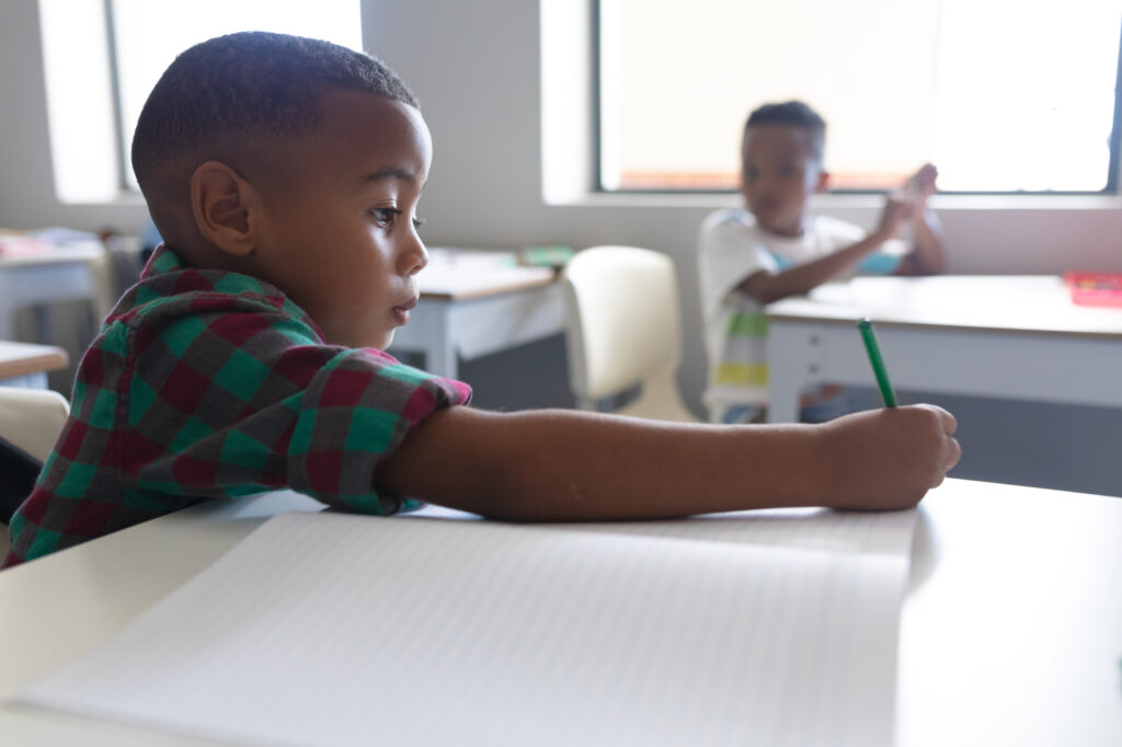 Cute African American elementary school boy writing in class.