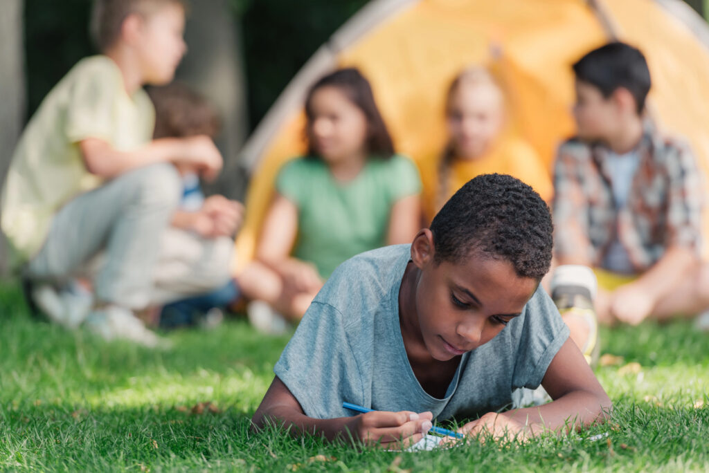 african american boy writing outdoors nature journal